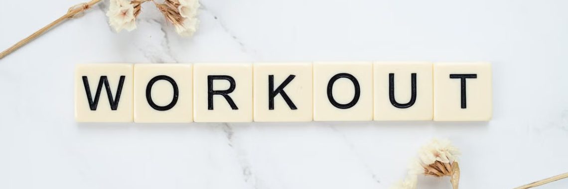 Letter tiles spelling 'WORKOUT' on marble with dried flowers, conveying fitness motivation.